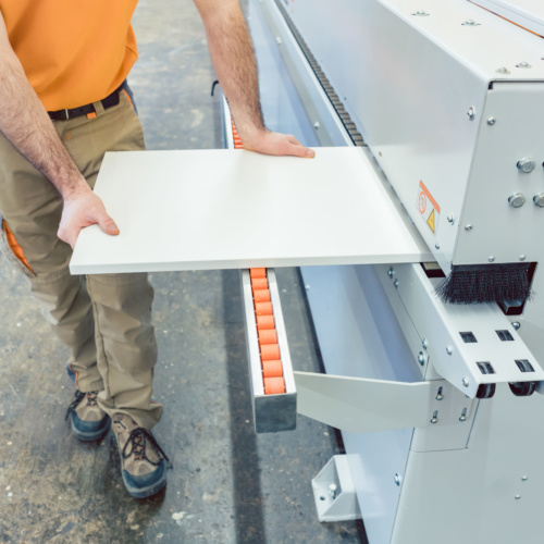 Carpenter in furniture factory working on veneer machine with great diligence